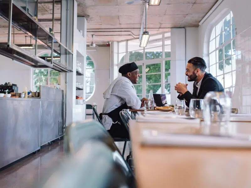 Man in suit talking to chef in restaurant.