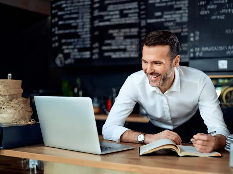 Smiling Manager using laptop behind restaurant counter.